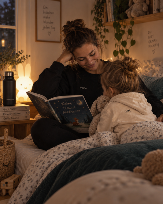 Mutter liest ihrem Kind im Bett vor, beide in JoisPulse Statement-Kleidung
