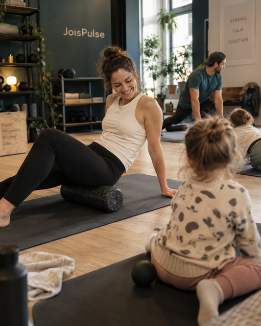 Frau auf der Matte beim Faszientraining, Kind sitzt daneben und schaut zu