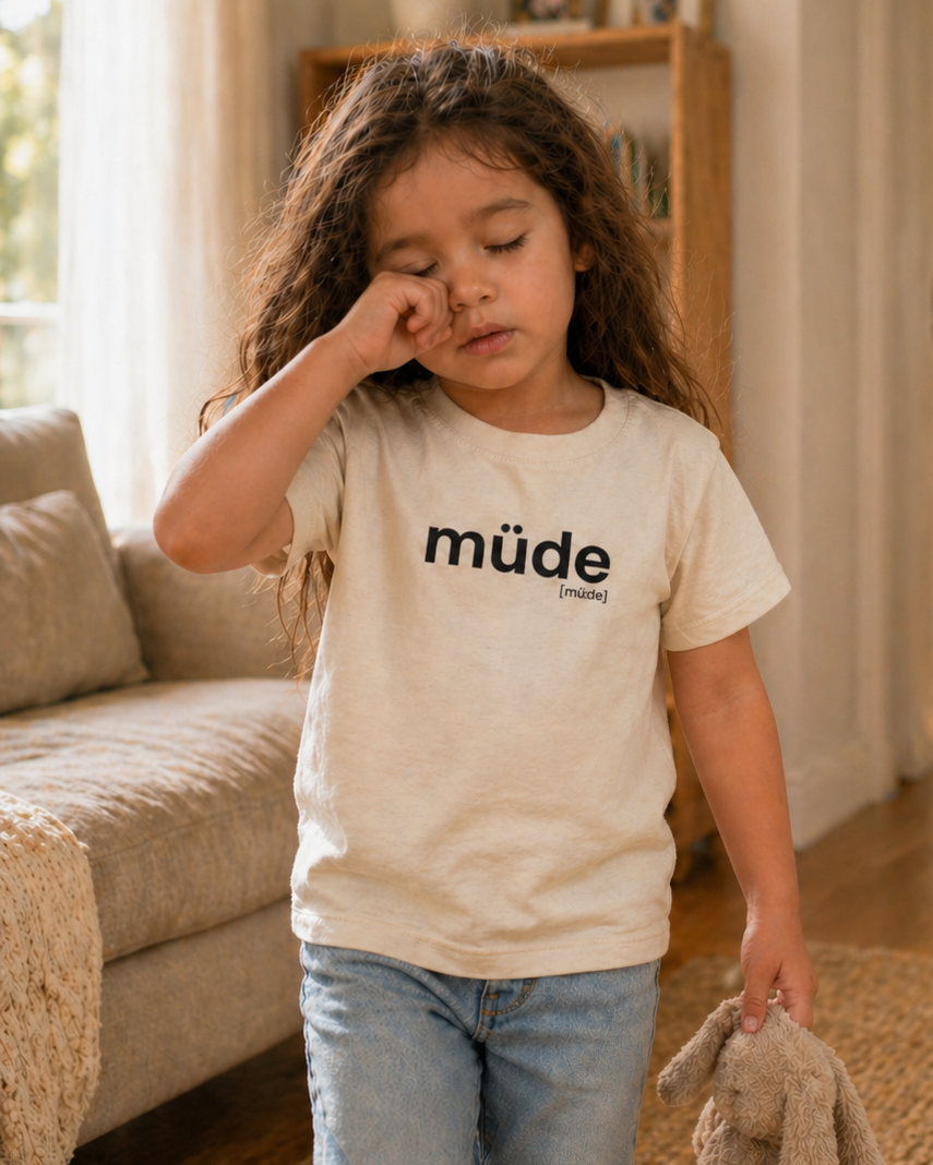 Mädchen im Wohnzimmer trägt das JoisPulse Kinder T-Shirt mit dem Statement müde