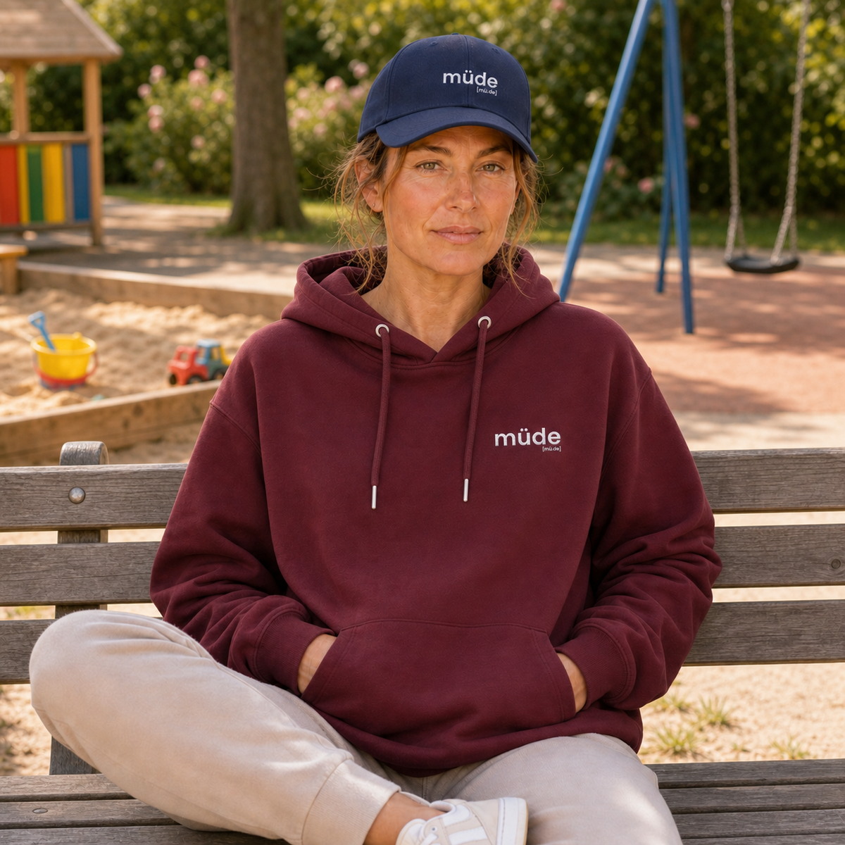 Frau sitzt auf einer Spielplatzbank im JoisPulse Hoodie mit dem Statement müde
