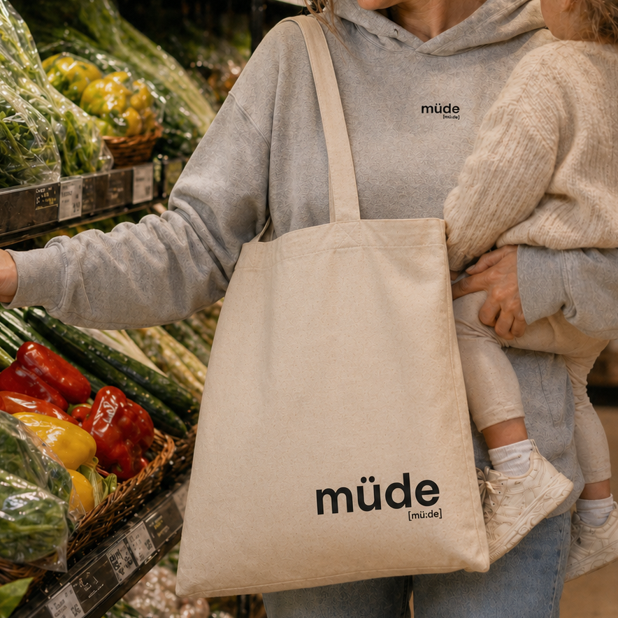 Mutter mit Kleinkind im Supermarkt trägt den JoisPulse Stoffbeutel mit dem Statement müde