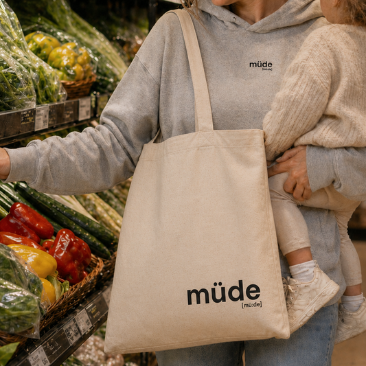 Mutter mit Kleinkind im Supermarkt trägt den JoisPulse Stoffbeutel mit dem Statement müde