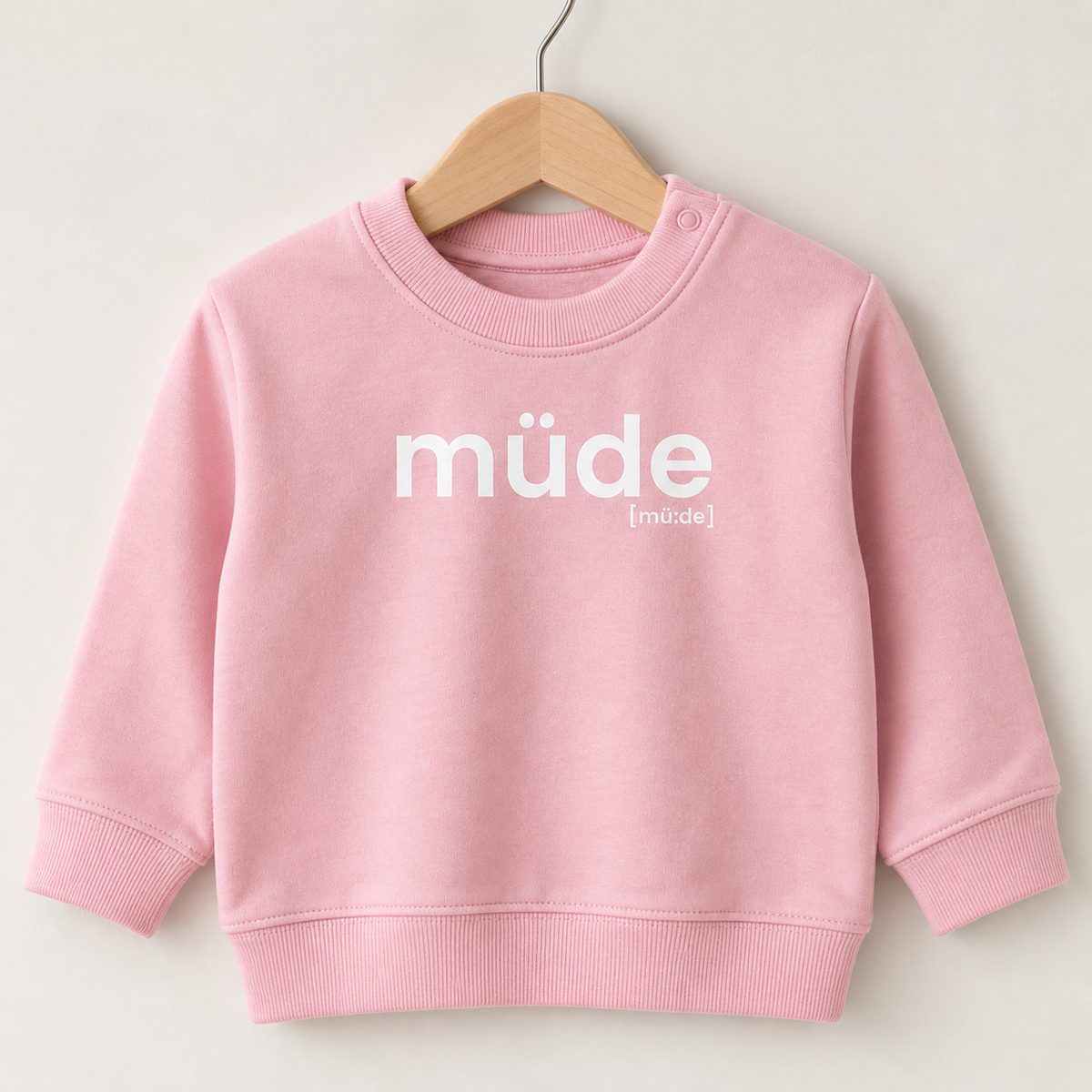 Rosafarbenes Baby Sweatshirt müde von JoisPulse auf einem Holzbügel