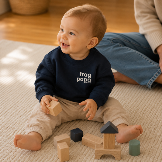 Baby spielt mit Holzbausteinen auf einem Teppich und trägt das dunkelblaue JoisPulse Baby Sweatshirt mit dem Statement frag papa