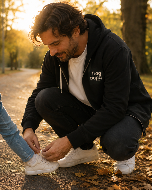 Vater bindet einem Kind auf einem Herbstweg den Schuh, trägt den schwarzen JoisPulse Zip-Hoodie mit dem Statement frag papa