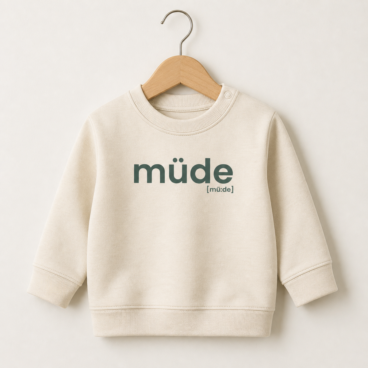 Cremefarbenes Baby Sweatshirt müde von JoisPulse auf einem Holzbügel