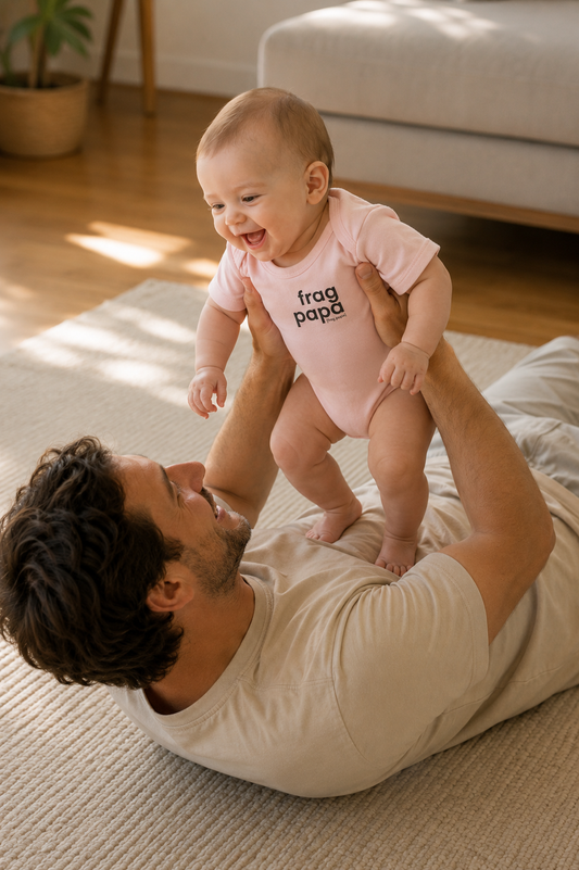 Vater hält sein lachendes Baby hoch, das Baby trägt den JoisPulse Body mit dem Statement frag papa
