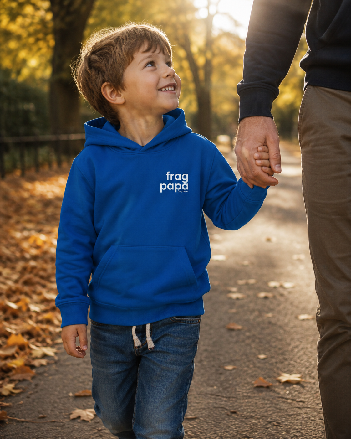Junge hält die Hand seines Vaters auf einem Herbstweg und trägt den blauen JoisPulse Kinder Hoodie mit dem Statement frag papa